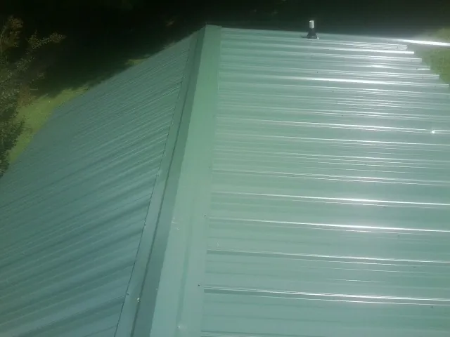 New green metal panels meeting at the ridge of a roof — Flat Roof Repair work by our crew in Panguitch