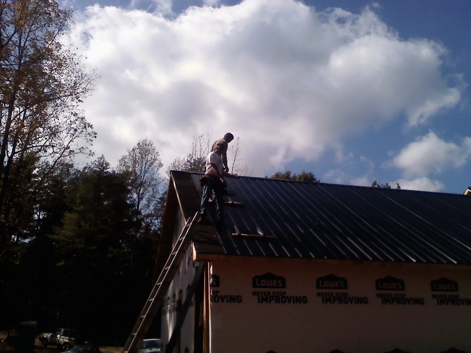 Roofer fastening dark metal panels high against a cloudy sky, from a Roof Inspection job in Panguitch