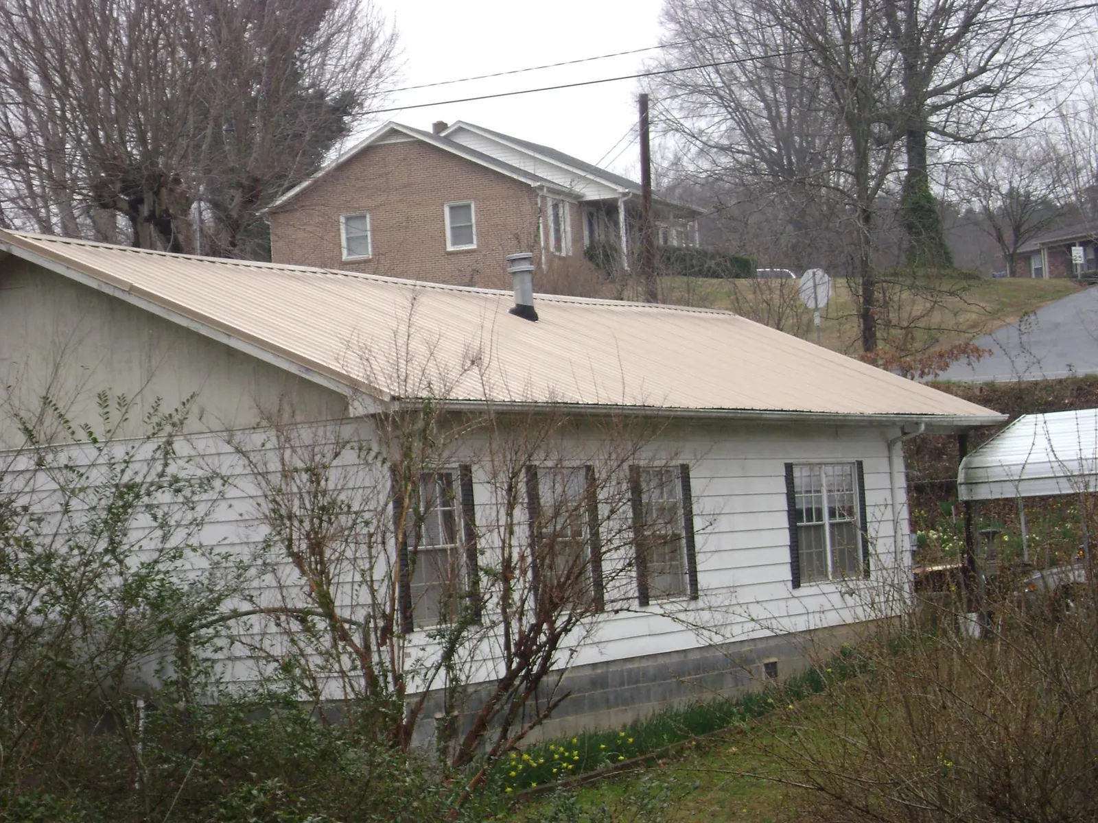 Tan metal roof on a white sided house set into a hillside — Commercial Roofing by Roofing Brothers in Panguitch